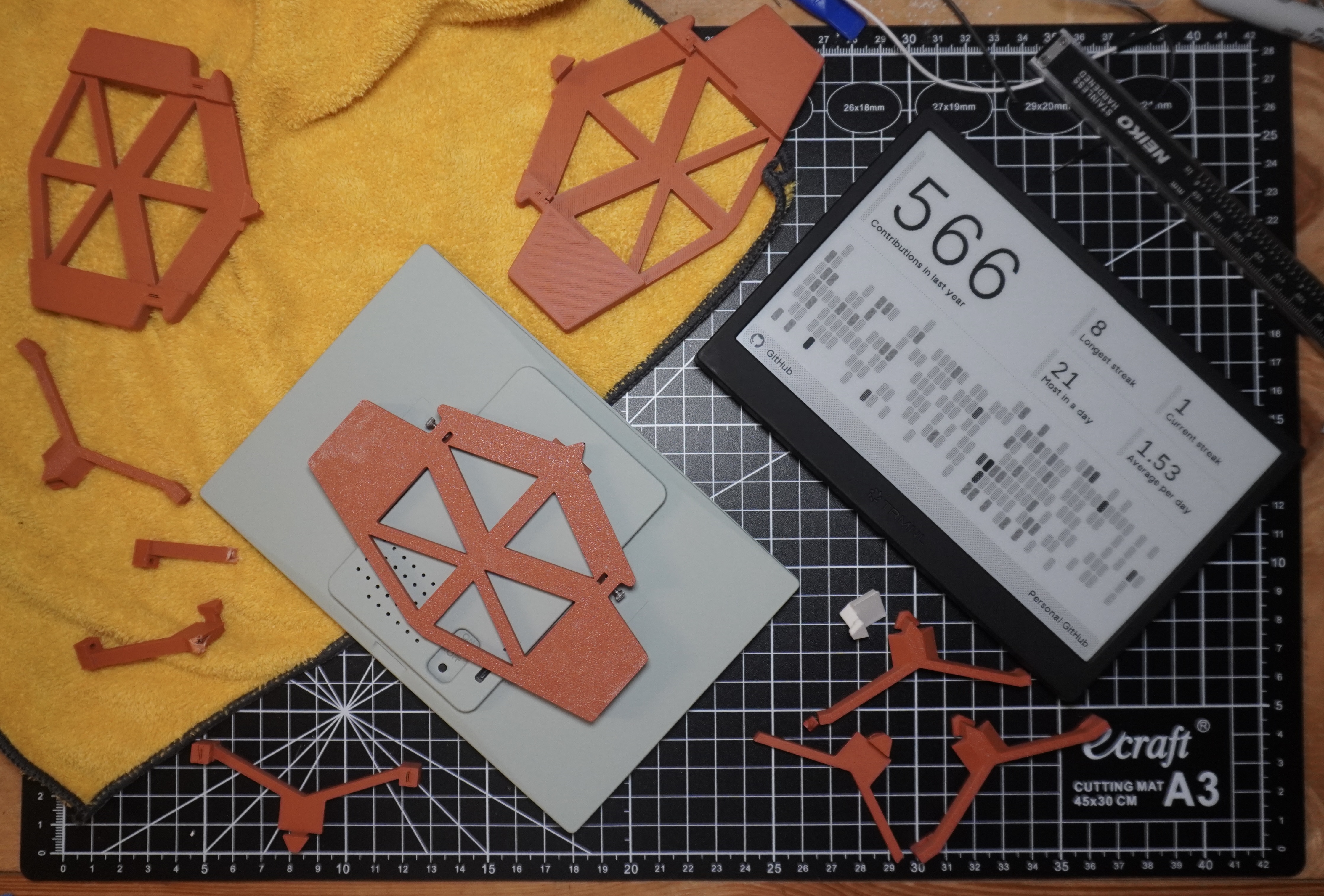 A collection of attempts A top down image of my two TRMNLs E-Ink devices on my workbench. One is displaying my Github statistics while the other has been flipped upside down to show the magnetic mount on the back. Scattered around the rectangular E-Ink displays are the various test prints I performed to dial in the design. This is all sitting atop a black, self-healing cutting mat.